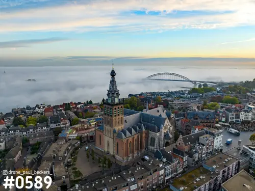 Luchtfoto van de Stevenskerk in Nijmegen met mist over de Waal en de Waalbrug op de achtergrond in ochtendlicht