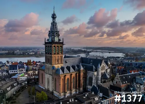 Luchtfoto van de Stevenskerk in Nijmegen met de Waal en de Waalbrug op de achtergrond onder roze avondwolken