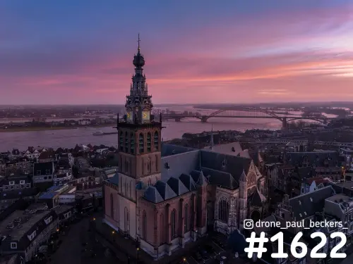 Luchtfoto van de Stevenskerk in Nijmegen met de Waal en de Waalbrug op de achtergrond onder een roze schemerlucht
