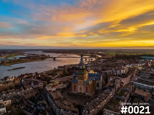 Luchtfoto van de Stevenskerk in het centrum van Nijmegen met de Waal en Waalbrug onder een gele en oranje avondhemel