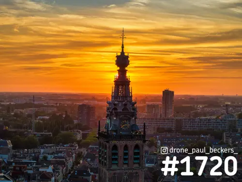 Luchtfoto van de Stevenskerk in Nijmegen bij zonsondergang, met de torenspits tegen een oranje lucht boven het centrum