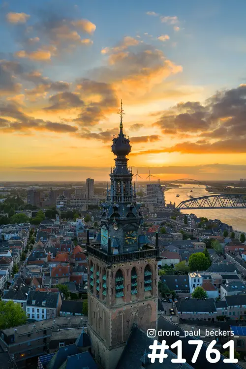 Luchtfoto van de Stevenskerk in Nijmegen bij zonsondergang, met oranje wolken en de Waal met brug op de achtergrond