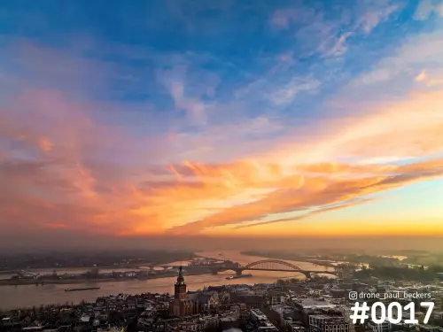 Luchtfoto van Nijmegen met de Stevenskerk en de Waalbrug aan de Waal onder een oranje en roze gekleurde wolkenlucht