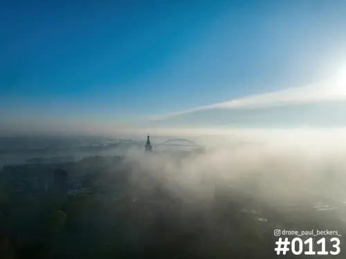 Luchtfoto van de Stevenskerk en de Waalbrug in Nijmegen, met dikke mist over de stad en laagstaande zon rechts