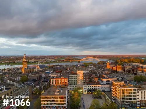 Luchtfoto van Nijmegen met de Stevenskerk en de Waalbrug over de Waal, laag zonlicht onder zware donkere wolken