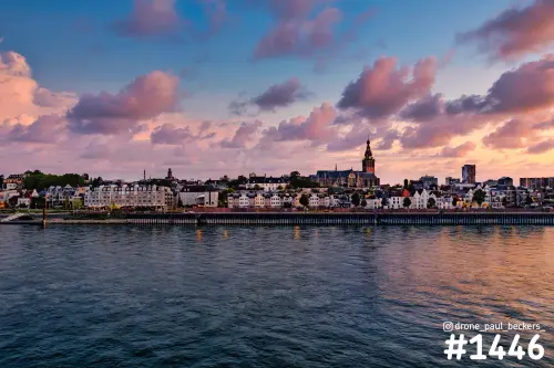 Stevenskerk en Waalkade in Nijmegen gezien over de Waal, met roze wolken boven de huizenrij aan het water