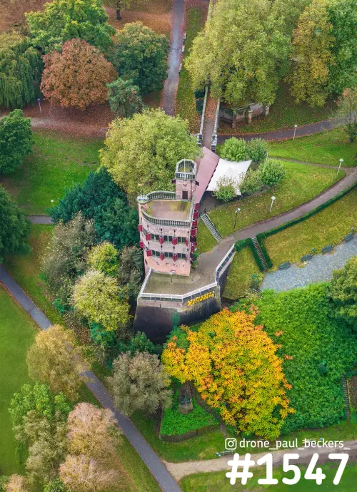Luchtfoto van een bakstenen toren in het Valkhof gebied in Nijmegen, omringd door herfstbomen in geel, oranje en groen