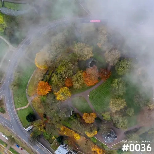 Luchtfoto van het Valkhofpark in Nijmegen in de herfst, met mist boven kleurende bomen en een gebogen weg eromheen