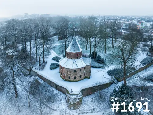 Luchtfoto van de besneeuwde Sint-Nicolaaskapel in het Valkhofgebied in Nijmegen, omringd door kale bomen en een muur