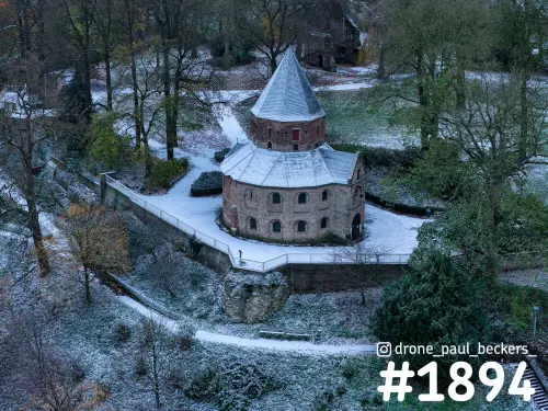 Luchtfoto van een ronde stenen kapel met kegeldak in het Valkhofgebied in Nijmegen, onder een dun laagje sneeuw