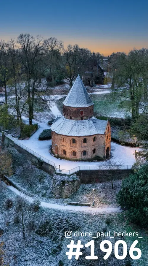 Luchtfoto van de ronde bakstenen kapel in het Valkhofgebied in Nijmegen, met sneeuw en een oranje gloed aan de horizon