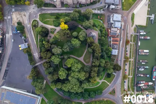 Luchtfoto recht van boven op het Valkhofpark in Nijmegen met kronkelende paadjes, een gele boom en de jachthaven aan de rechterkant