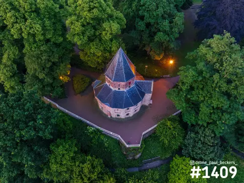 Luchtfoto van de Sint-Nicolaaskapel op het Valkhof in Nijmegen, schemering met oranje lantaarnlicht tussen de bomen