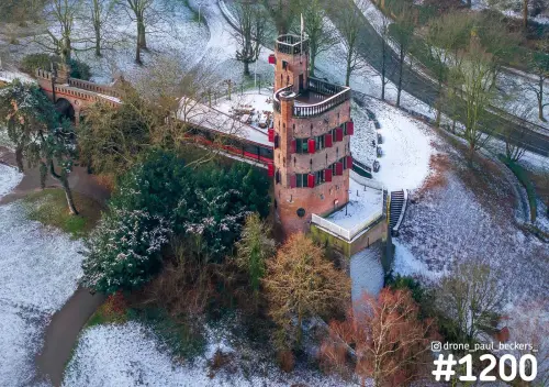 Luchtfoto van een bakstenen toren met rode luiken in het Valkhof gebied in Nijmegen, met sneeuw op de paden en kale bomen