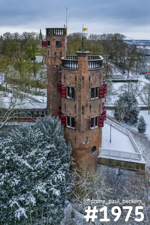 Luchtfoto van een bakstenen toren met rode luiken in het Valkhofgebied in Nijmegen, omringd door besneeuwde bomen