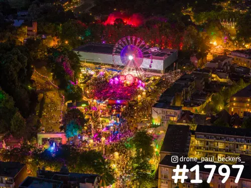 Luchtfoto van de Vierdaagsefeesten in Nijmegen bij nacht, met reuzenrad en een drukke menigte tussen gekleurde lichten