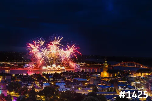 Luchtfoto van vuurwerk boven de Waal in Nijmegen in de avond, met de verlichte Stevenskerk en de Waalbrug rechts