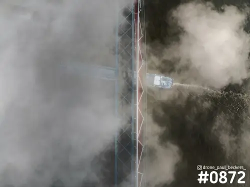 Luchtfoto recht van boven van een stalen brug over de Waal met een schip dat in de mist onder de brug vaart