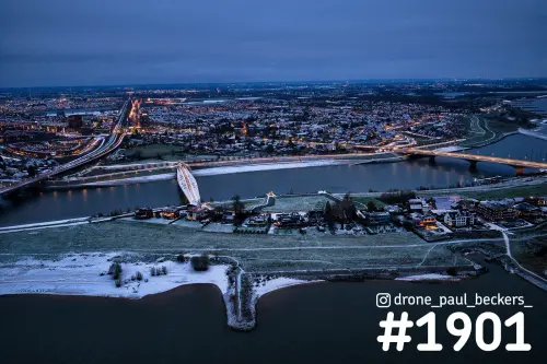 Luchtfoto van de Waal en de nevengeul bij Lent in Nijmegen in het blauwe uur, met sneeuw op de oever en stadslichten