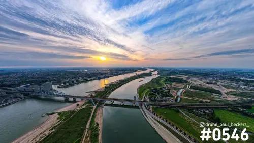 Luchtfoto van de Waal bij Nijmegen met de nevengeul en een brug onder een wolkenlucht en laagstaande zon
