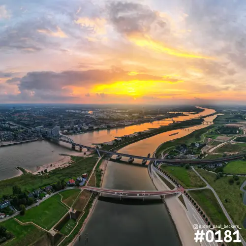 Luchtfoto van de Waal bij Nijmegen tijdens zonsondergang, met brug over de nevengeul en oranje lucht boven de rivier