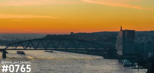 Luchtfoto van de Waal in Nijmegen met een stalen boogbrug en hoogbouw aan de Handelskade onder een oranje schemerlucht