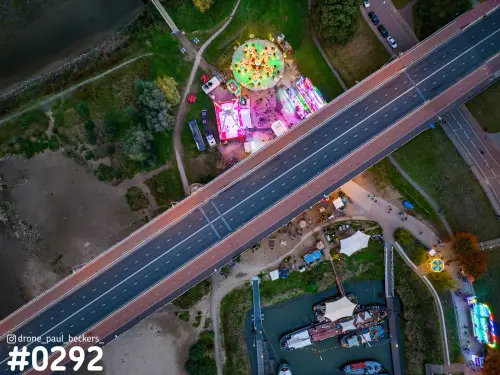 Luchtfoto van de kermis aan de Waal in Nijmegen in de avondschemering, met brug en boten in de Lindenberghaven