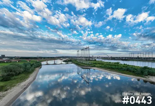Luchtfoto van de Waal en nevengeul in Nijmegen met wolkenlucht weerspiegeld in het water en De Oversteek in de verte