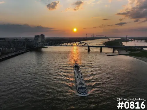 Luchtfoto van een binnenvaartschip op de Waal bij Nijmegen met de brug De Oversteek tegen een zonsondergang