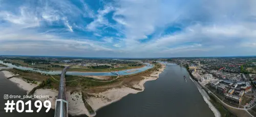 Panoramafoto van de Waal bij Nijmegen vanaf de Waalbrug, met zandbanken langs de oever, de stad rechts en een wolkenlucht
