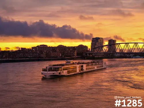 Rivierschip op de Waal in Nijmegen bij zonsondergang, met oranje lucht en een stalen boogbrug naast de Waalkade