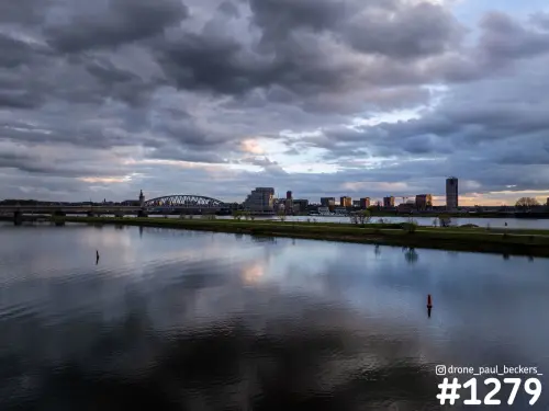 Luchtfoto van de Waal en de skyline van Nijmegen onder zware wolken, met rode boeien in het spiegelende water