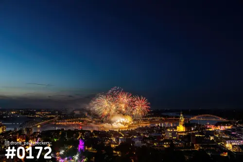 Luchtfoto van vuurwerk boven de Waal in Nijmegen, met de verlichte Stevenskerk en de Waalbrug in de blauwe avondlucht