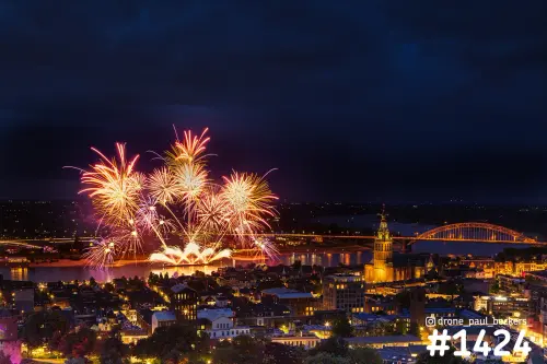 Luchtfoto van vuurwerk boven de Waal in Nijmegen, met de verlichte Stevenskerk en de Waalbrug in de avond