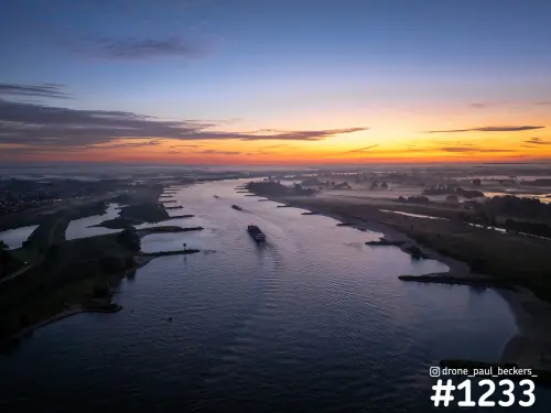 Luchtfoto van de Waal bij de Ooijpolder bij zonsopkomst, met een binnenvaartschip op het water en mist boven de uiterwaarden