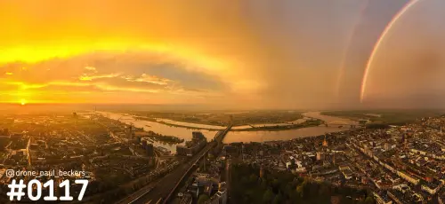 Luchtfoto van de Waal en de Waalbrug in Nijmegen met laagstaande zon en een dubbele regenboog boven de stad