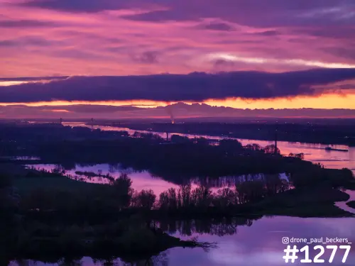 Luchtfoto van de Waal bij Weurt in de schemering, met paarsroze wolken boven overstroomde uiterwaarden en een schip op de rivier