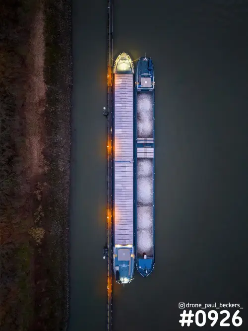 Luchtfoto van twee afgemeerde schepen langs een steiger aan de Waal bij Weurt, avondlicht met oranje lampen