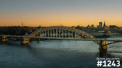 Luchtfoto van de Waalbrug in Nijmegen bij zonsondergang, met oranje avondlucht boven de rivier de Waal en het centrum