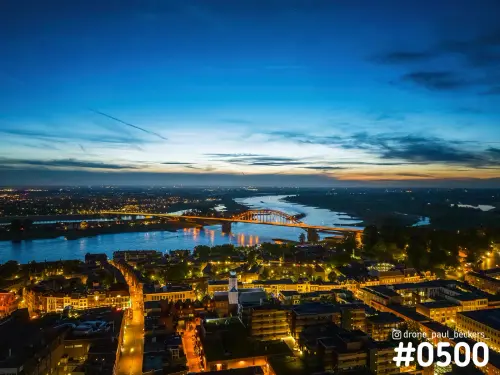 Luchtfoto van het centrum van Nijmegen met de verlichte Waalbrug over de Waal in het blauwe uur na zonsondergang
