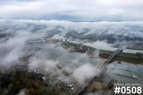 Luchtfoto van de Waalbrug in Nijmegen met lage mist boven de Waal, schepen op de rivier en herfstbomen op de oever