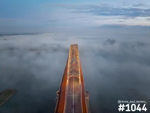 Luchtfoto van de Waalbrug in Nijmegen in schemerlicht, met laaghangende mist boven de Waal en een oranje verlichte brug