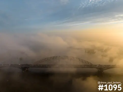 Luchtfoto van de Waalbrug in Nijmegen met dikke mist boven de rivier de Waal en een gouden gloed aan de horizon