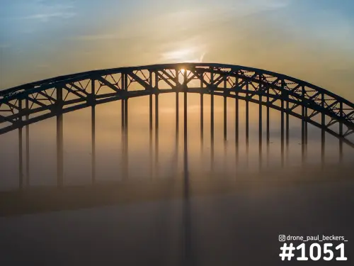 Boogbrug van de Waalbrug in Nijmegen als silhouet in dichte mist, met de zon die door de stalen constructie schijnt