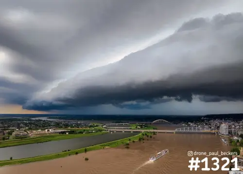 Luchtfoto van een donkere onweerswolk boven de Waal en de Waalbrug in Nijmegen, met een schip op het bruine water