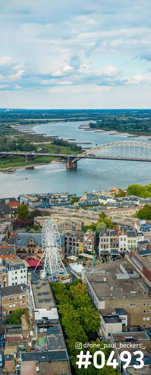 Luchtfoto van de Waalbrug in Nijmegen met een reuzenrad op de kermis, de rivier de Waal en daken van de binnenstad