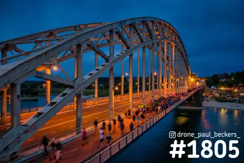 Wandelaars van de Vierdaagse op de Waalbrug in Nijmegen in het blauwe uur, met verlichte boogconstructie en de Waal ernaast