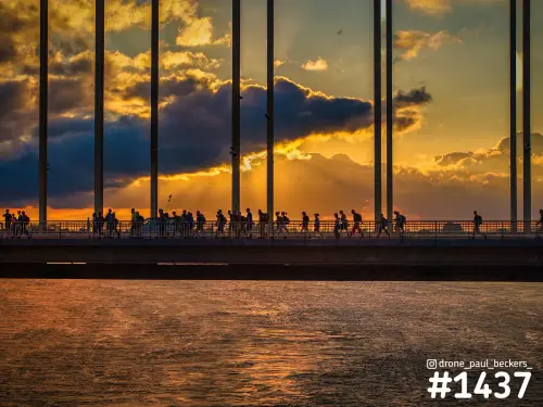Silhouetten van wandelaars van de Vierdaagse op de Waalbrug in Nijmegen tegen een oranje zonsondergang boven de Waal