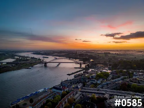 Luchtfoto van de Waalbrug in Nijmegen met oranje schemerlucht en roze wolken boven de Waal en de Waalkade