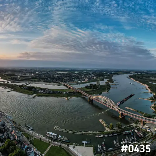 Luchtfoto van de Waalbrug over de Waal in Nijmegen in schemerlicht, met wolkenlucht, boten in de haven en zandbanken